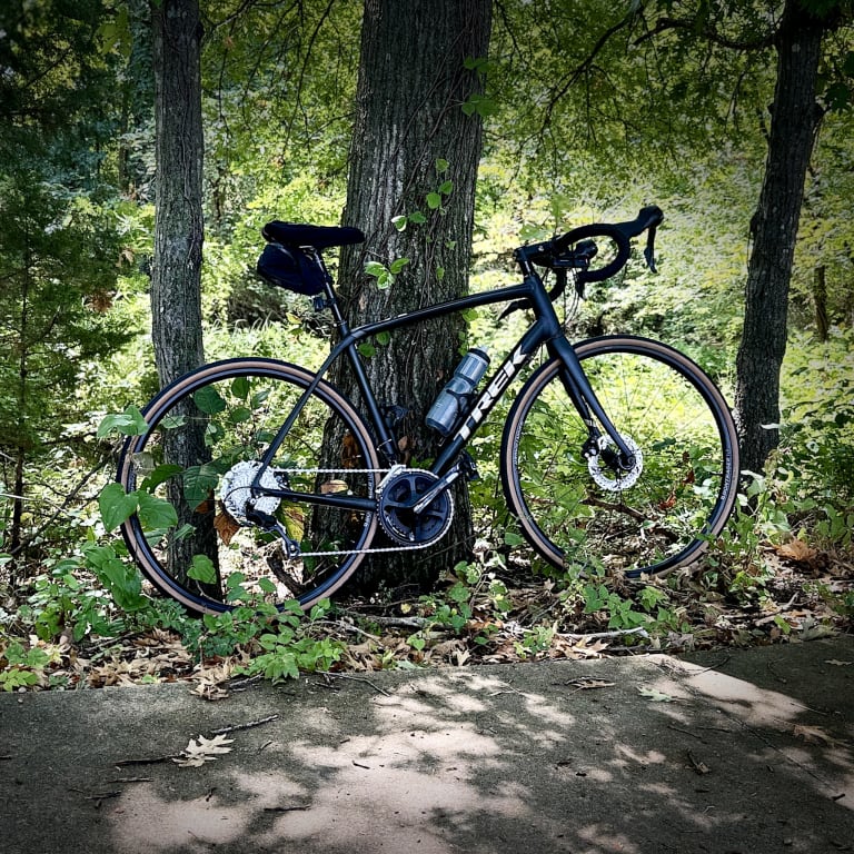 Black road bike on Bontrager tires leaning on a tree