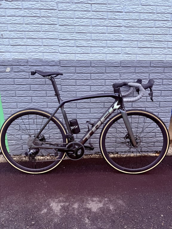 Gray road bike with tan-wall Bontrager tires against a white brick wall